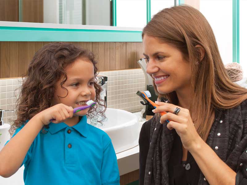 Woamn showing young girl how to brush her teeth both are smiling